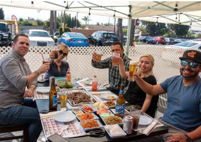 Five people toast drinks around a table of Korean barbecue dishes at an outdoor restaurant.