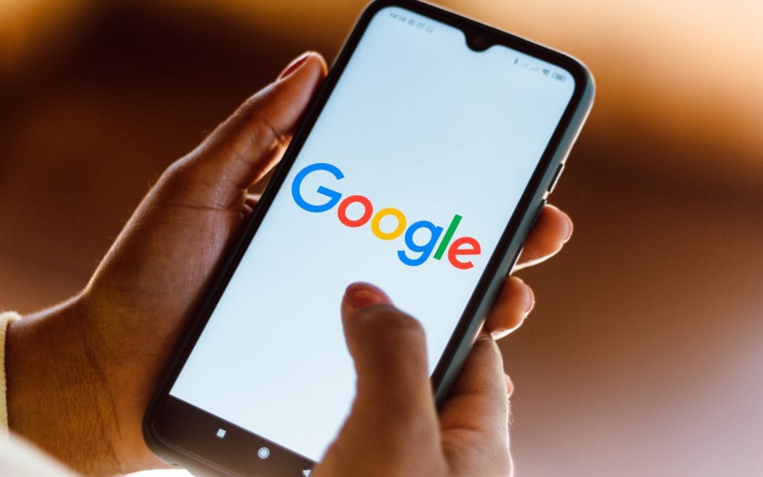 A person holding a smartphone with the Google logo displayed on the screen.