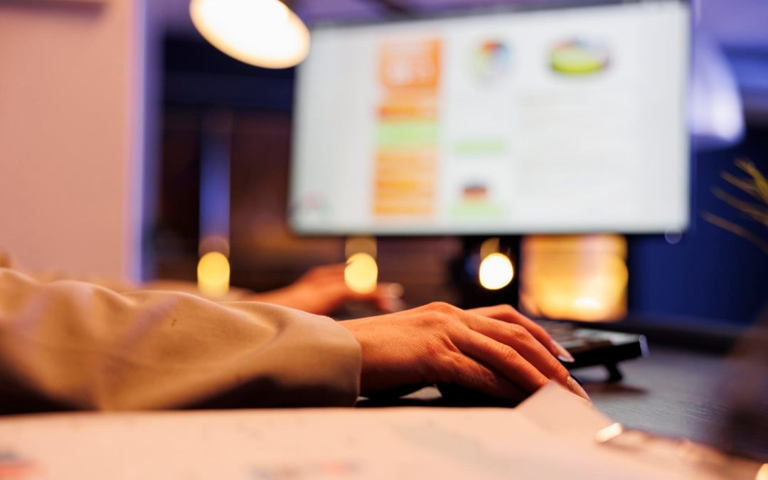 Person using a computer mouse at a desk with a blurred monitor in the background.